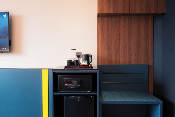 Una habitación moderna con cafetera integrada, un refrigerador pequeño y un armario de madera.