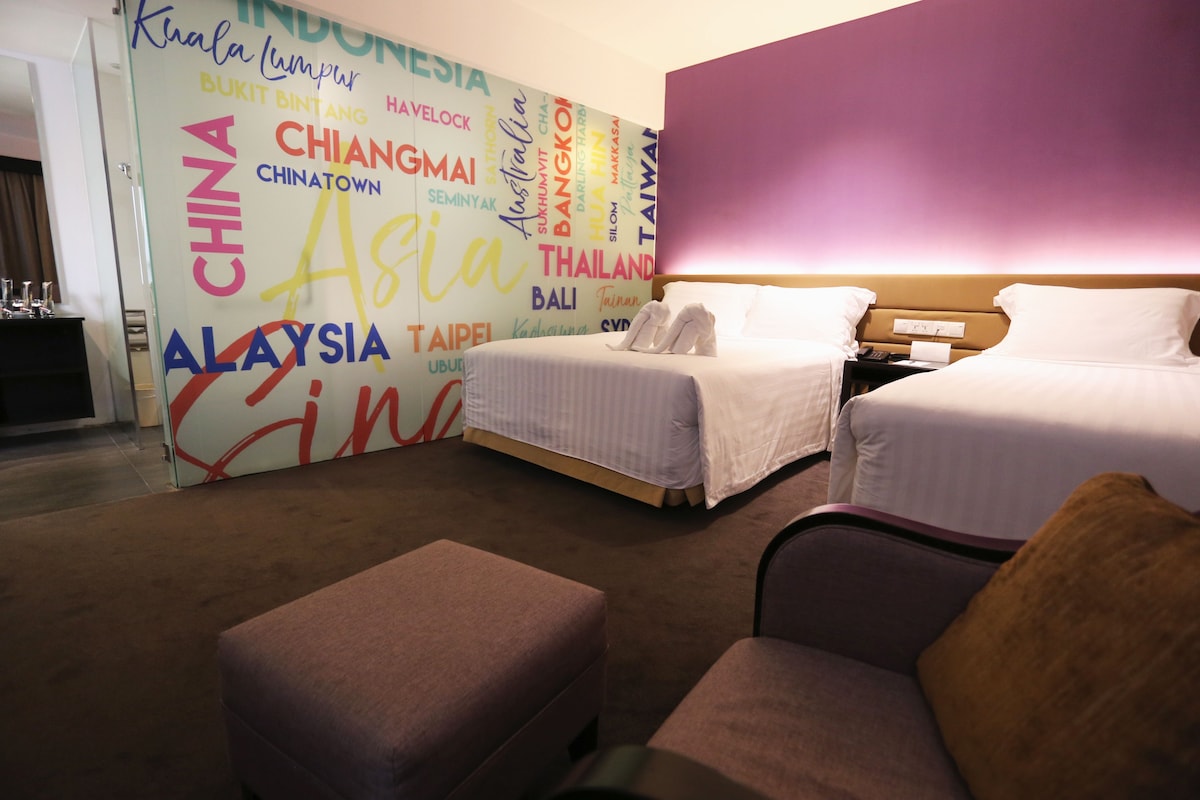 Habitación de hotel con dos camas, un sofá y una pared que muestra nombres de ciudades.