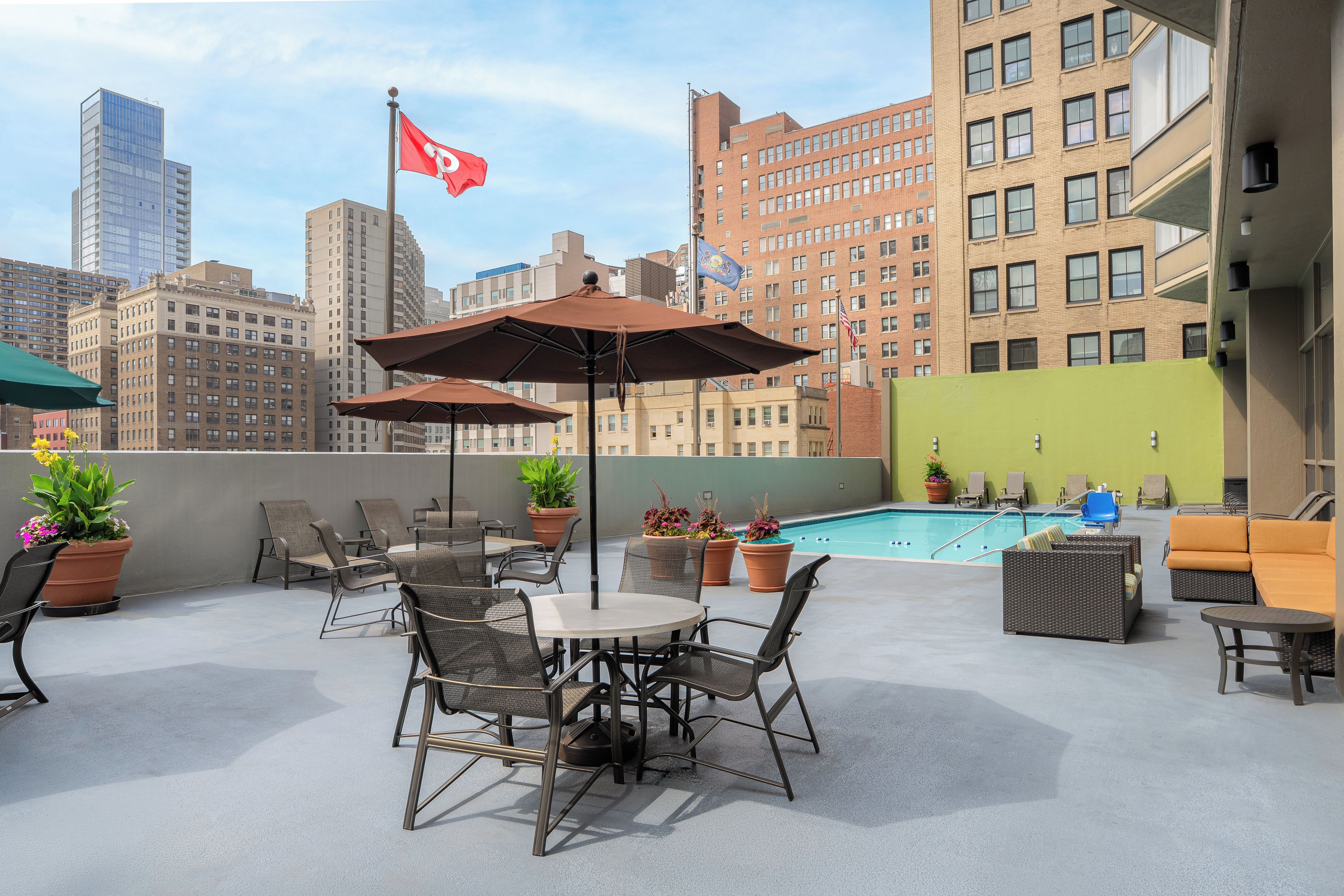 A rooftop terrace with outdoor seating, a pool, and city buildings in the background.