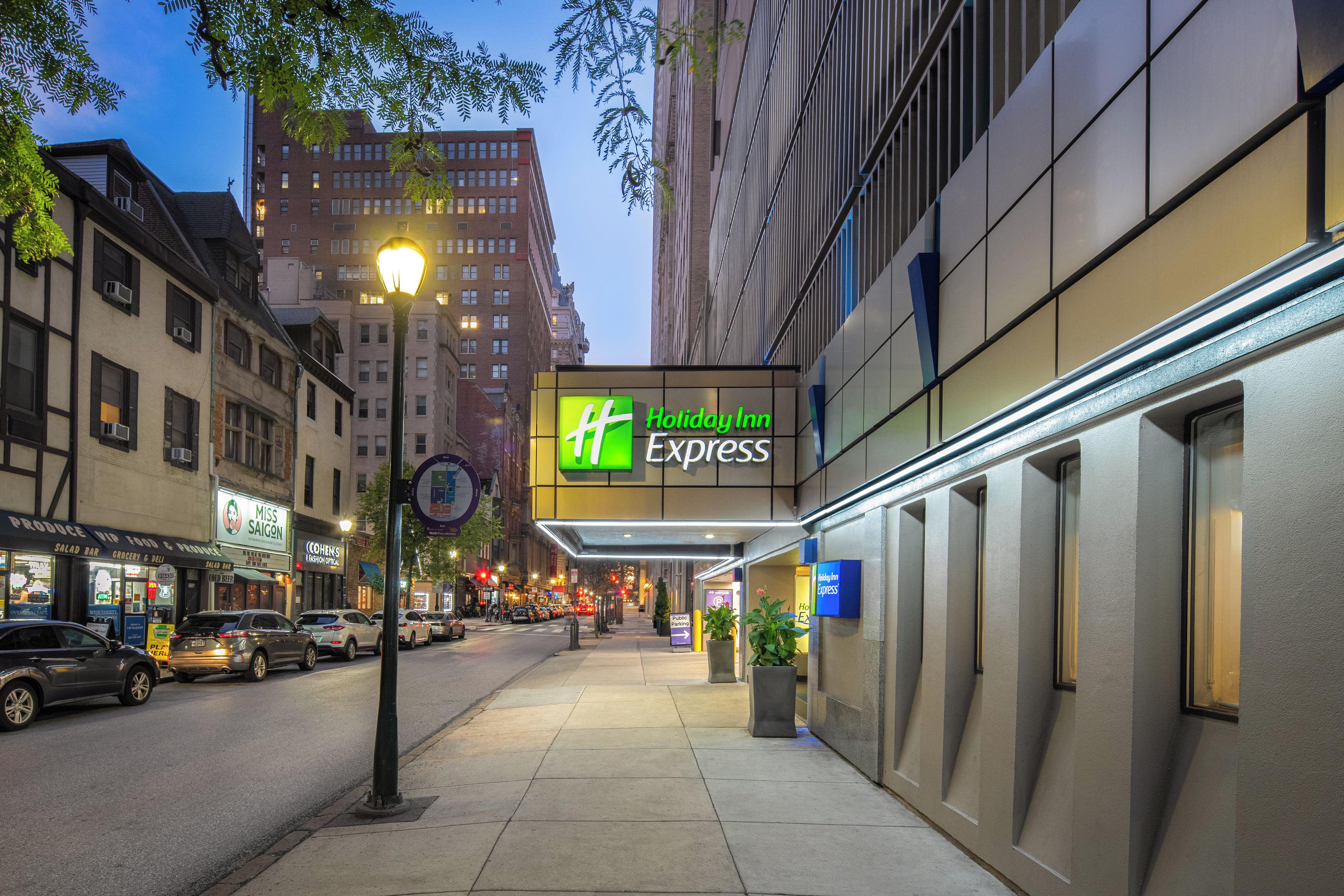A Holiday Inn Express with a prominent sign, located on a city street with buildings and parked cars.