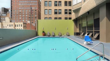 A rooftop pool with a clear blue pool, a green wall, and a row of lounge chairs.