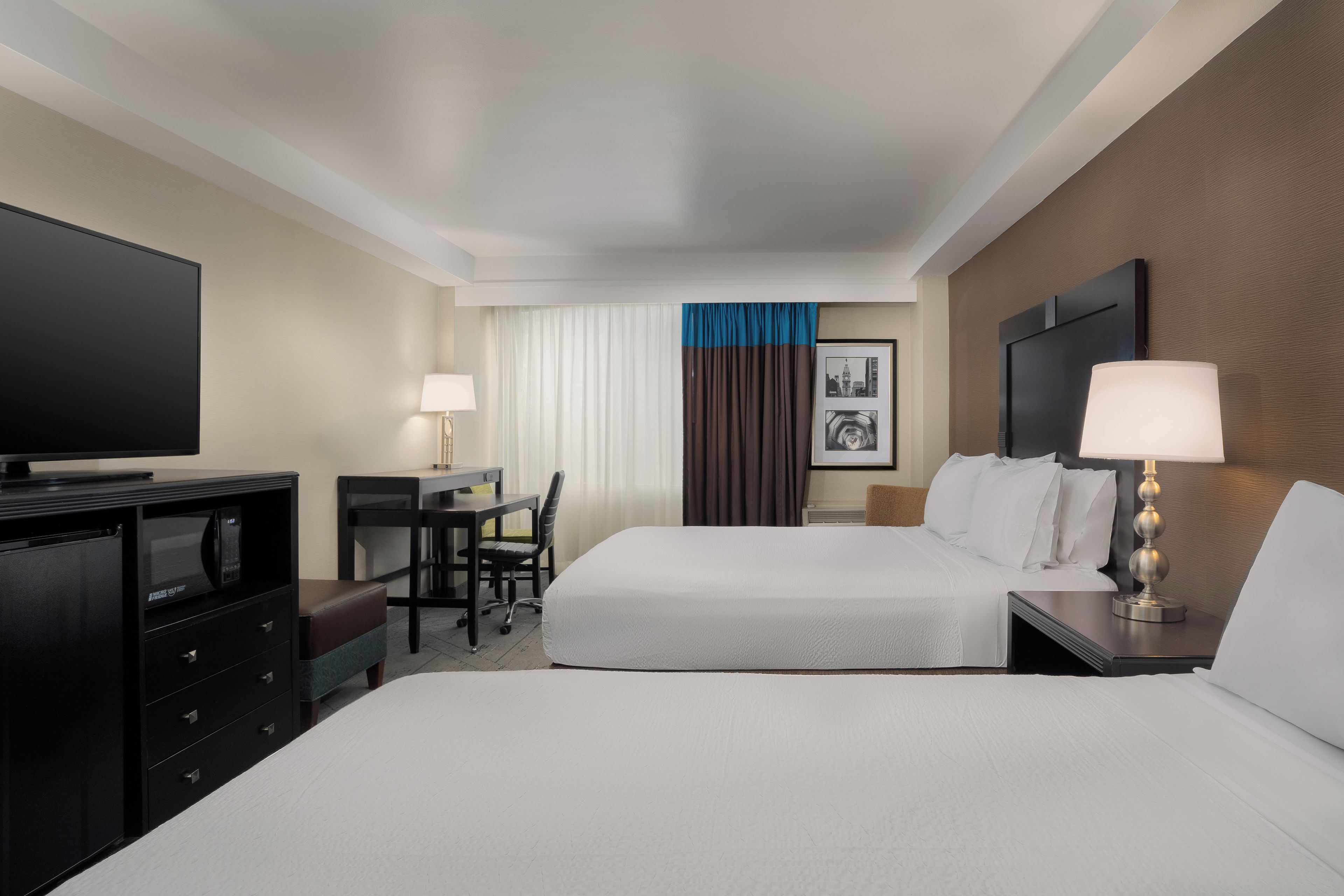 A hotel room with a bed, desk, chair, television, and lamps.