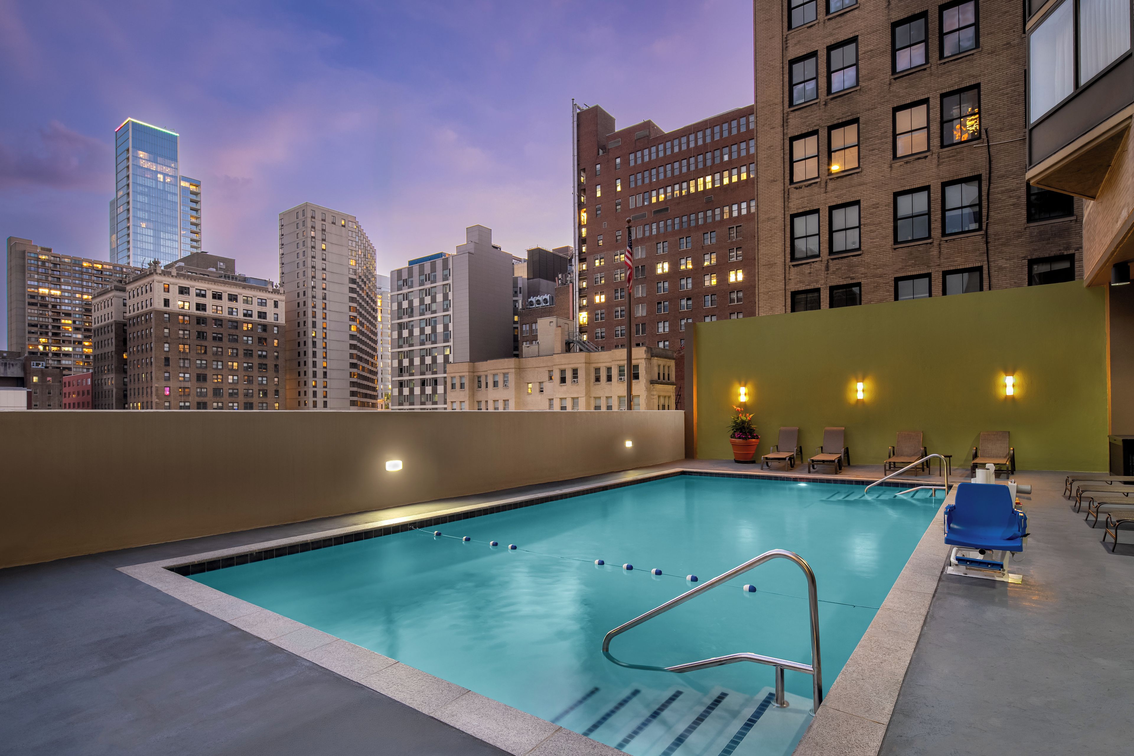 A rooftop pool with a city skyline view, lounge chairs, and a flag.