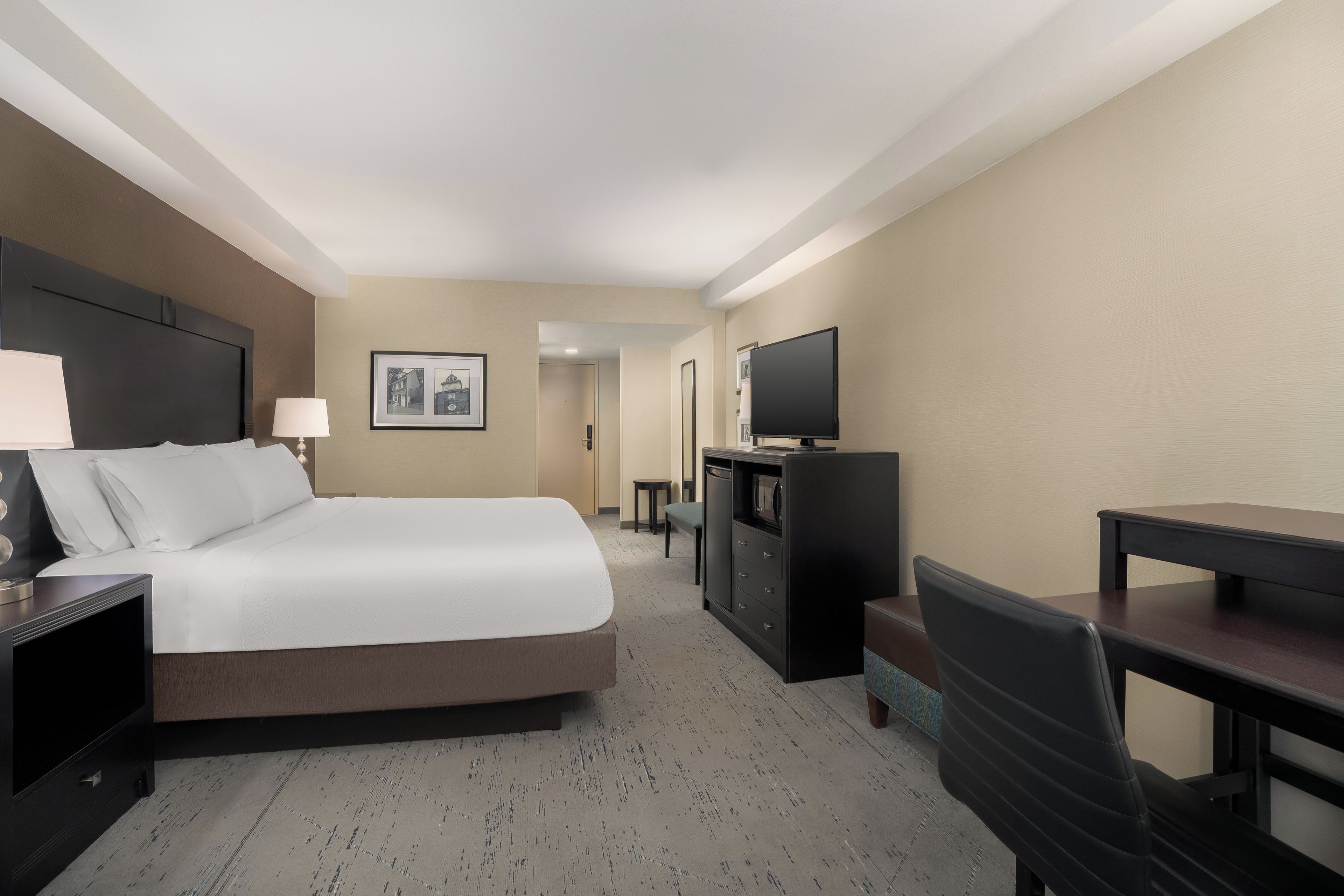 Una habitación de hotel con cama, escritorio, televisor y una silla.