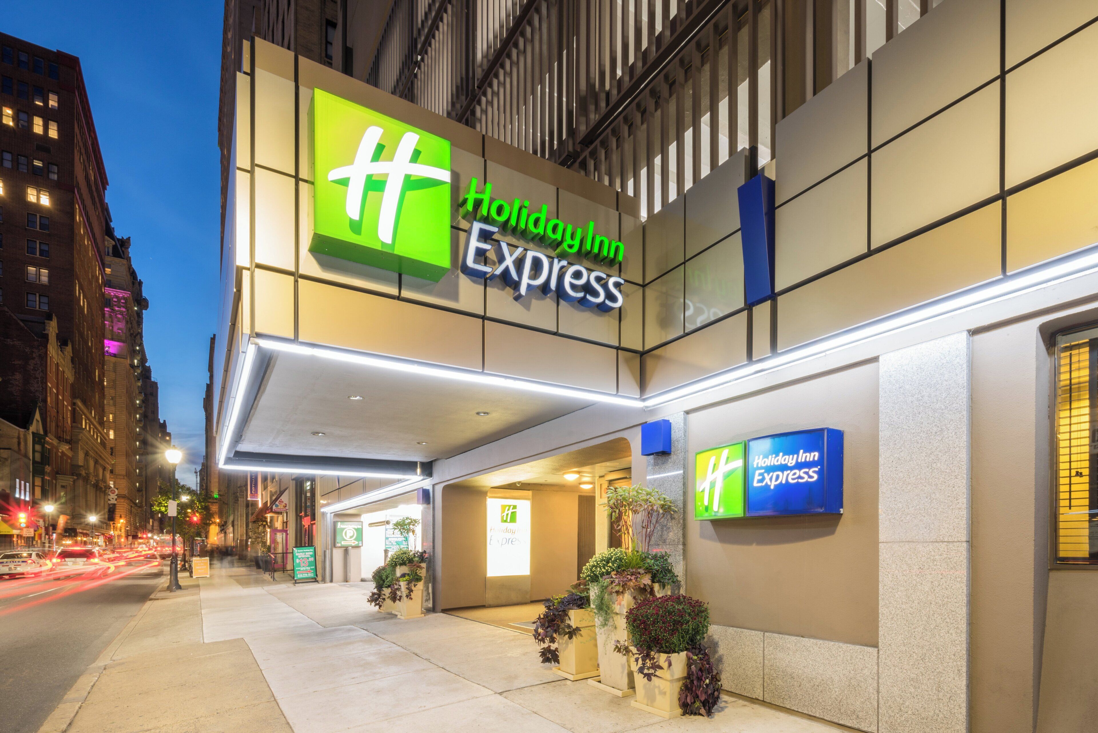 Um hotel Holiday Inn Express com uma placa visível, entrada coberta e plantas em vasos.