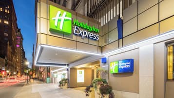 Um hotel Holiday Inn Express com uma placa visível, entrada coberta e plantas em vasos.