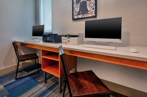 Uma mesa de escritório moderna com dois monitores, uma impressora e um teclado. Há duas cadeiras e uma estante.