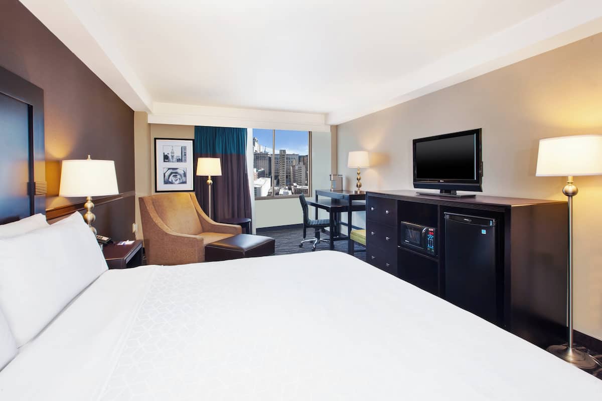 Una camera d'albergo con un letto grande, una scrivania con una sedia, una televisione, un minibar e vista sulla città.