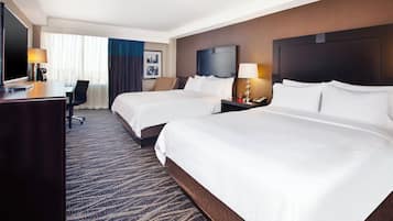 A hotel room with two beds, a desk, a chair, a TV, and a carpeted floor.