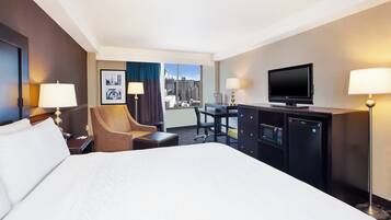 Una camera d'albergo con un letto grande, una scrivania con una sedia, una televisione, un minibar e vista sulla città.