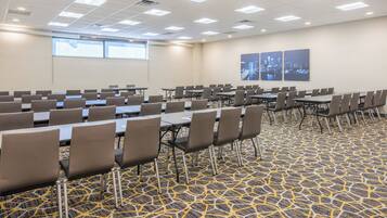 A conference room with rows of tables and chairs, carpeted floor, and a cityscape view.
