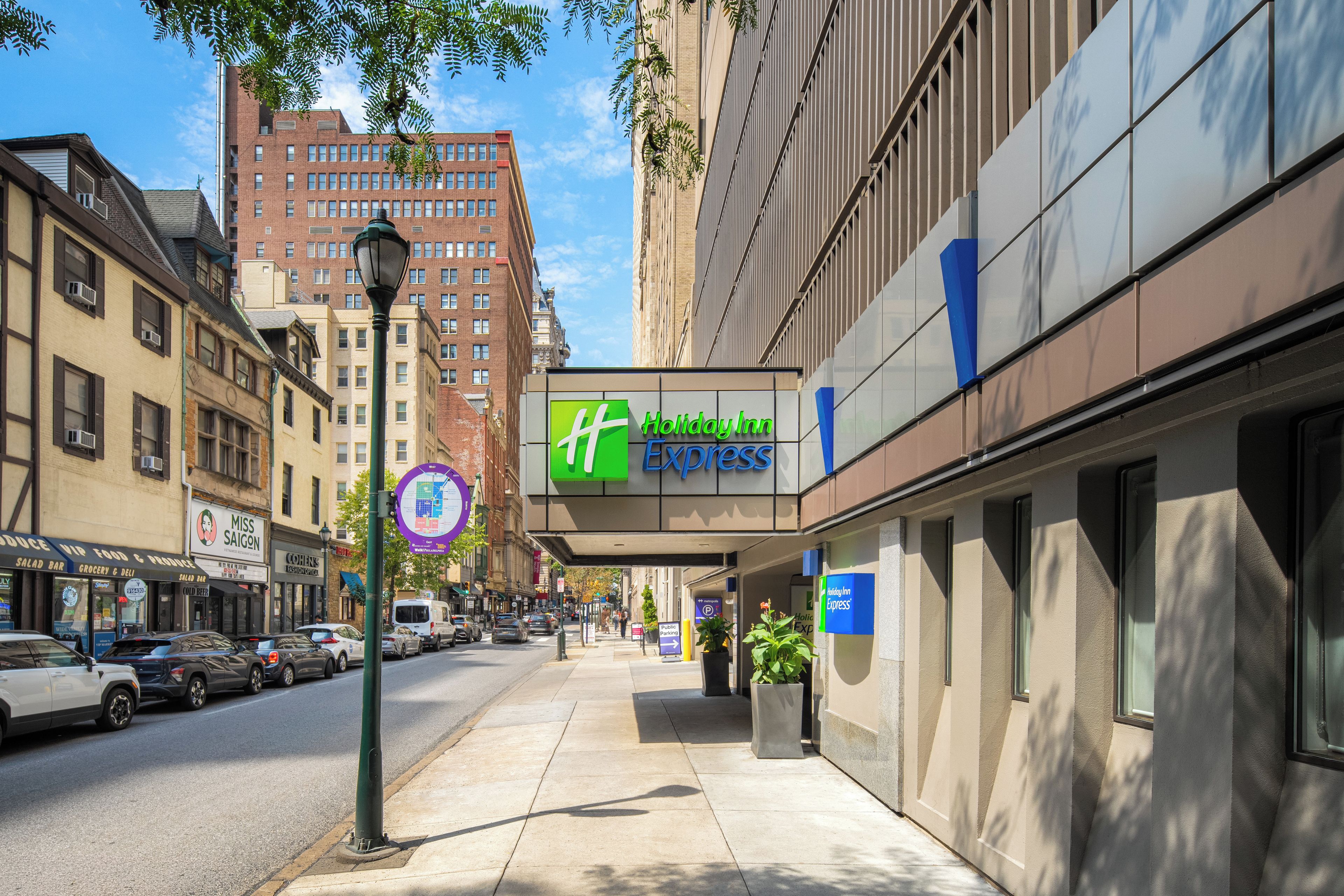 A street view with a Holiday Inn Express building, a sidewalk, parked cars, and surrounding buildings.