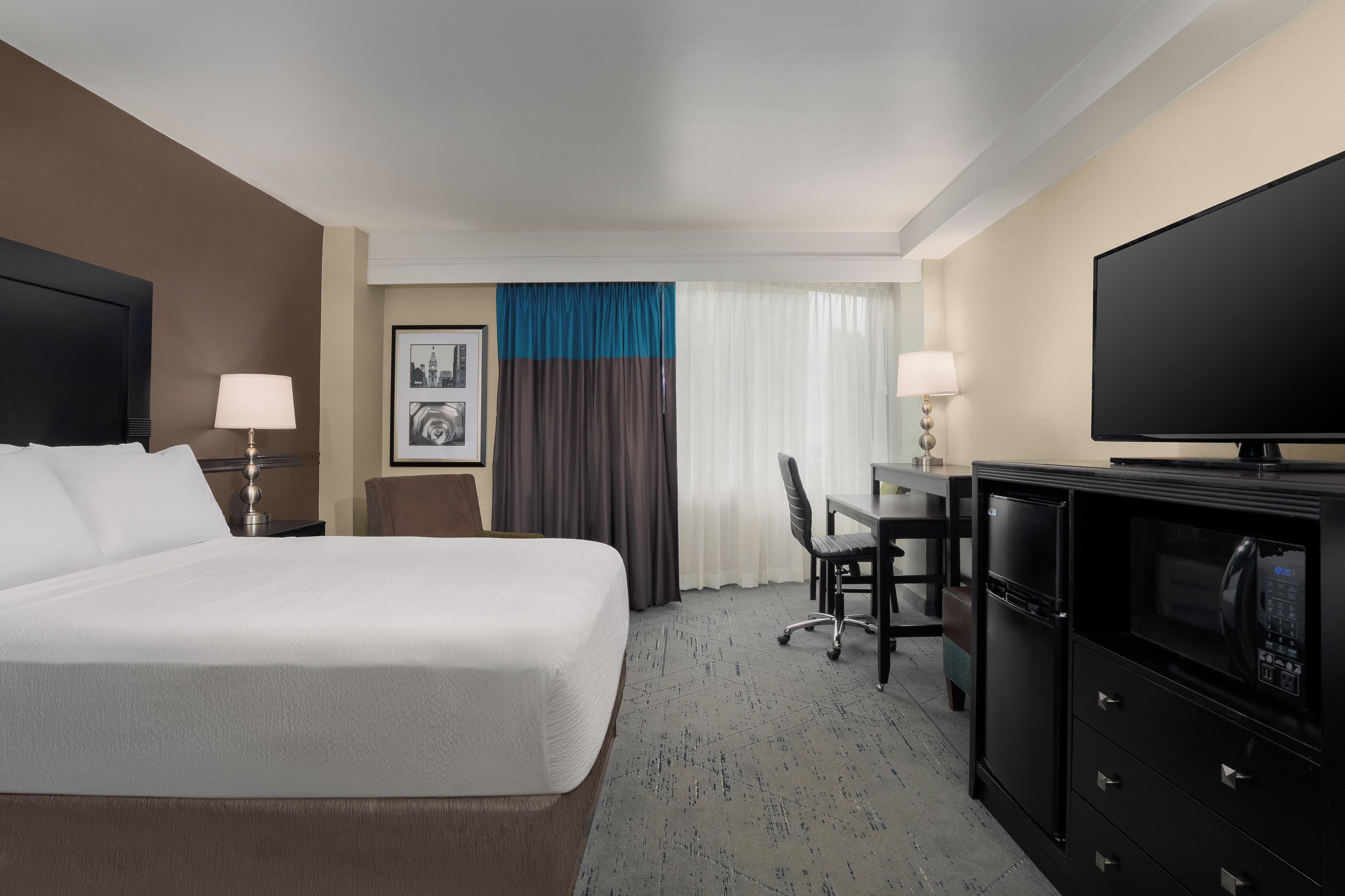 Una habitación de hotel con una cama, escritorio, televisor y minibar.