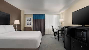Una habitación de hotel con una cama, escritorio, televisor y minibar.