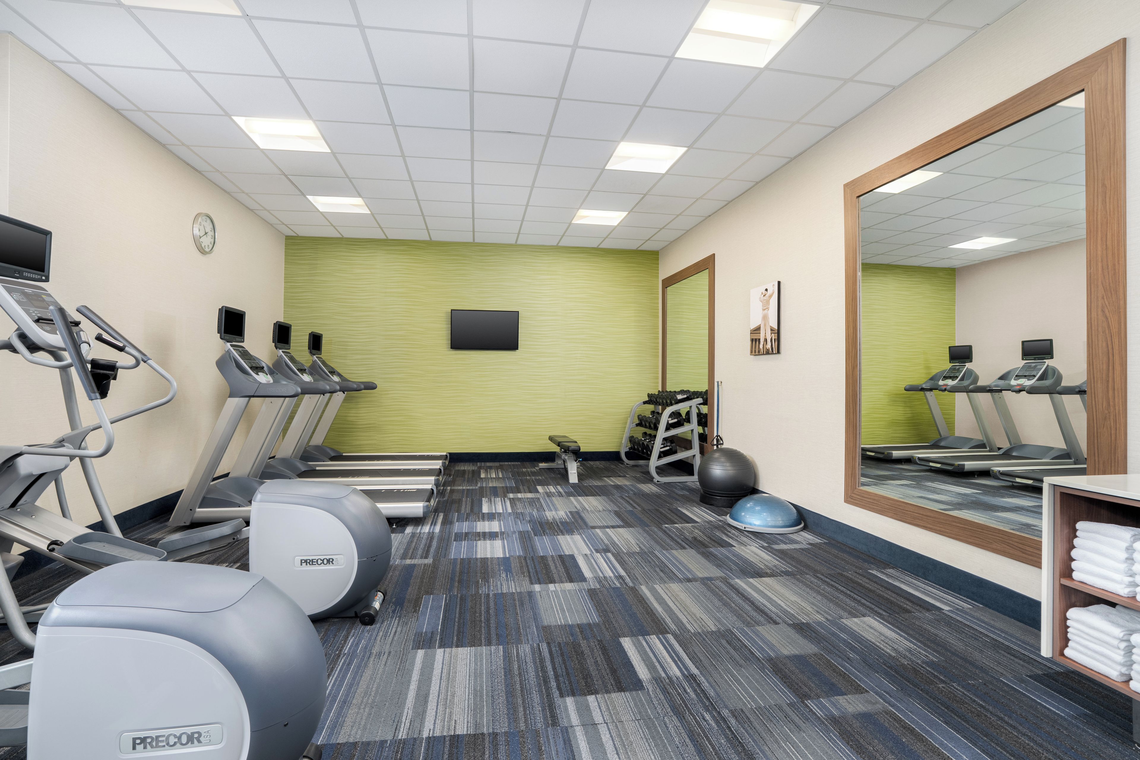 Une salle de sport équipée de tapis de course, de ballons d’exercice et d’un mur recouvert de miroirs.