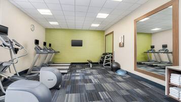 Une salle de sport équipée de tapis de course, de ballons d’exercice et d’un mur recouvert de miroirs.