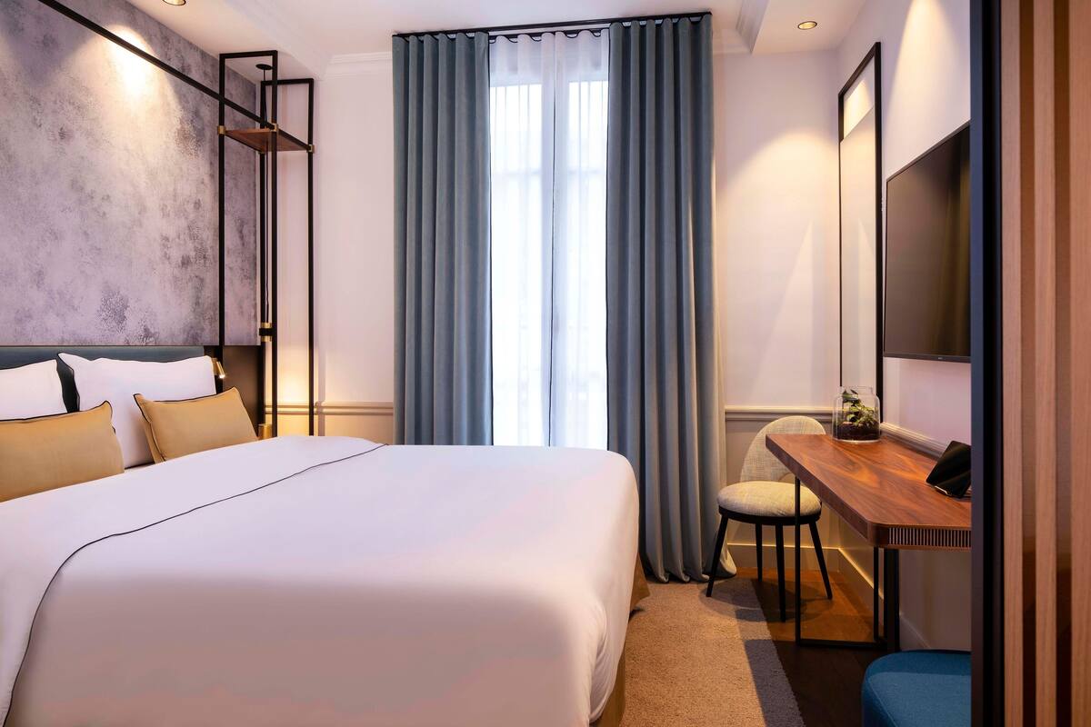 A modern hotel room with a large bed, a desk, and a TV.