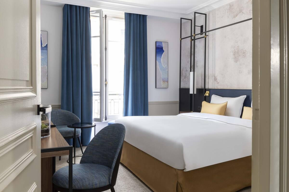 A hotel room with a bed, a desk, a chair, and a view of the outdoors.