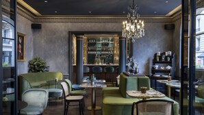 A modern interior with green upholstered seating, a bar area with shelves of bottles, and a chandelier.