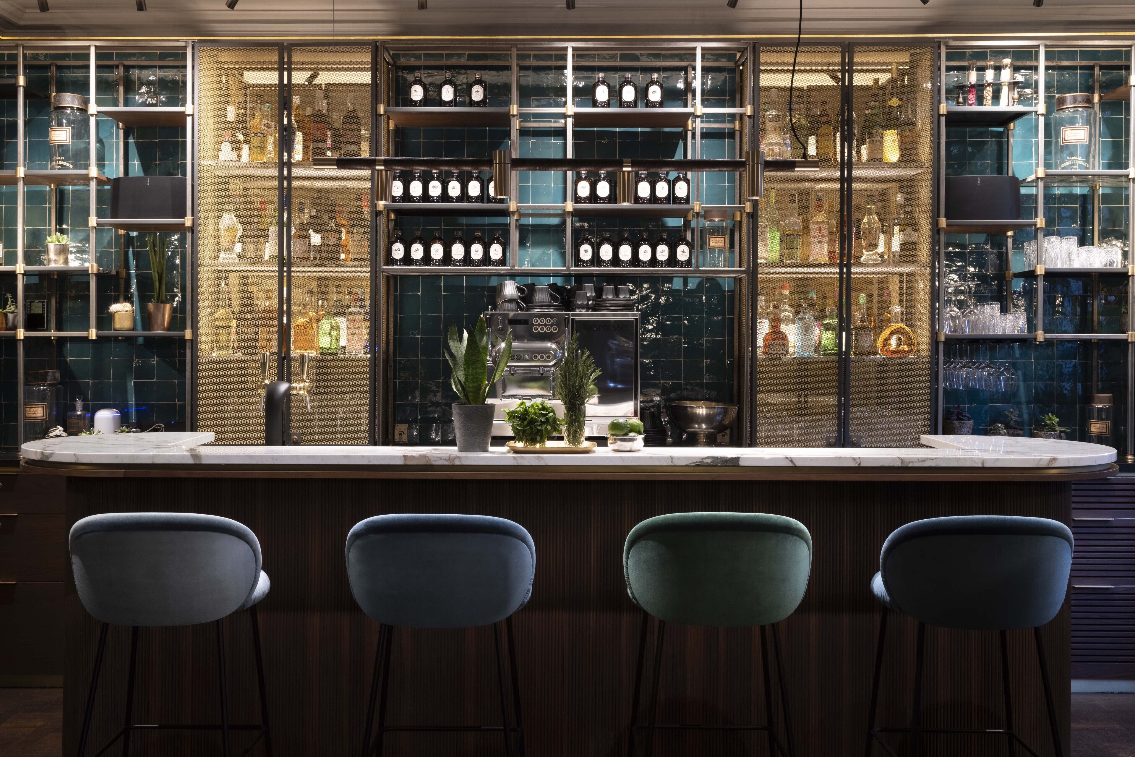 A bar area with a counter, shelves with bottles, and three bar stools.
