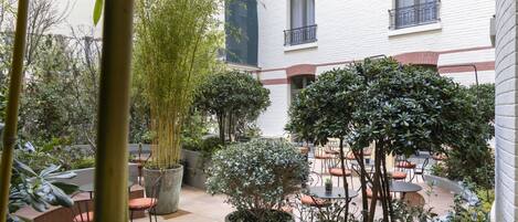 An outdoor patio area with tables and chairs, surrounded by potted plants and trees.