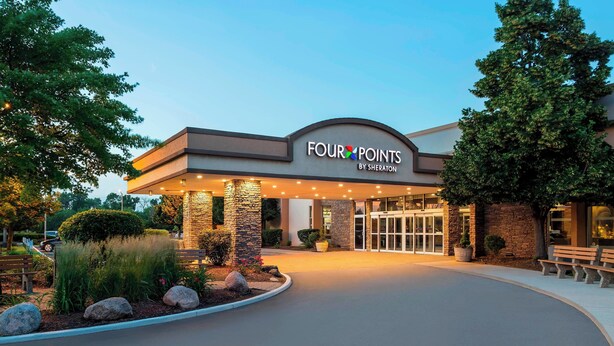 En hotellentrén med en skylt som visar texten ”FOUR POINTS BY SHERATON”, med en modern design som inkluderar stenpelare och ett välvt tak.