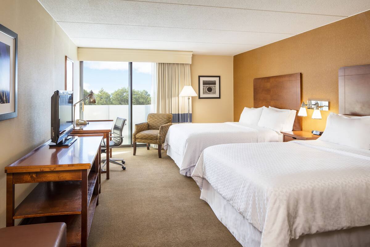 A hotel room with two beds, a desk, a chair, and a TV.