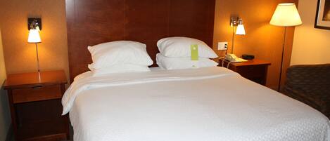 Una habitación de hotel con una cama grande, dos mesitas de noche y dos lámparas de pared.