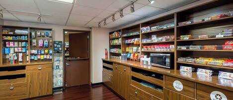 A well-lit store with wooden shelves stocked with various products, including snacks and household items. There are clear signs for trash and recycling bins.
