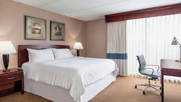 A hotel room with a large bed, two bedside lamps, a desk with a chair, and a window with curtains.