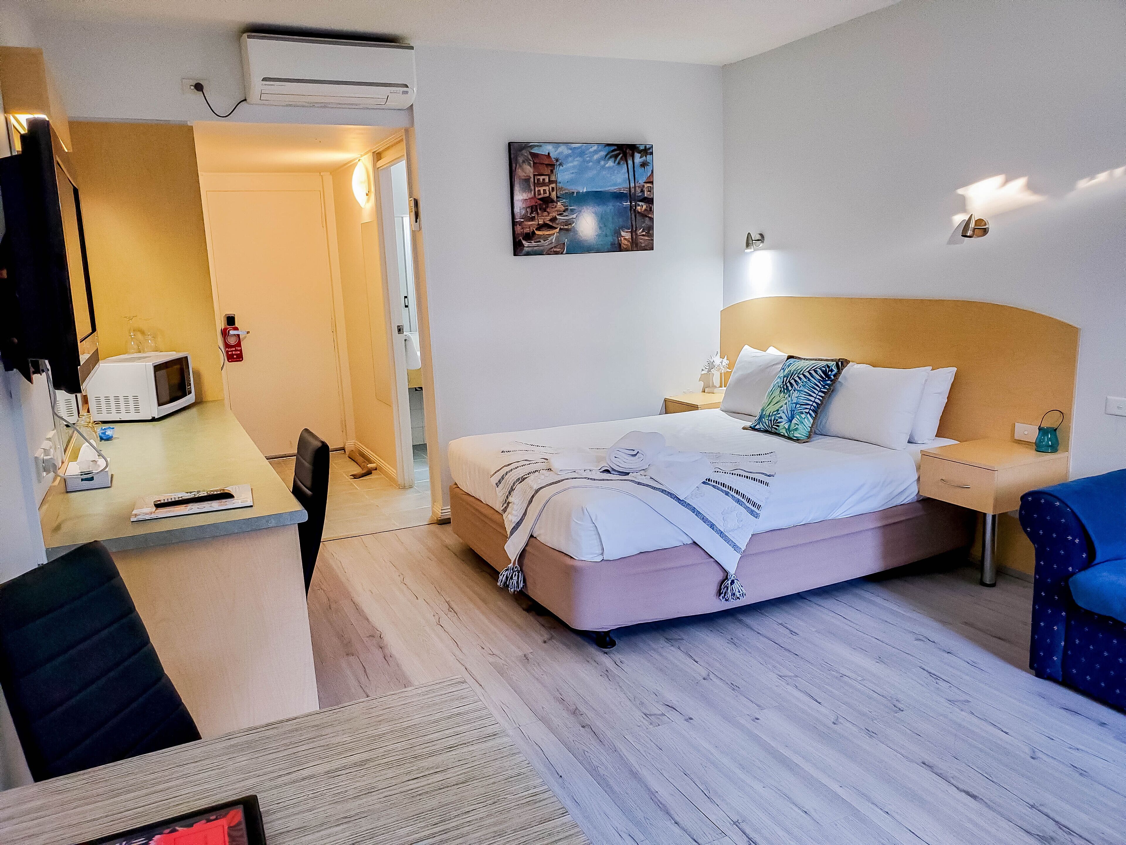 A hotel room with a bed, bedside table, chair, and a painting on the wall.