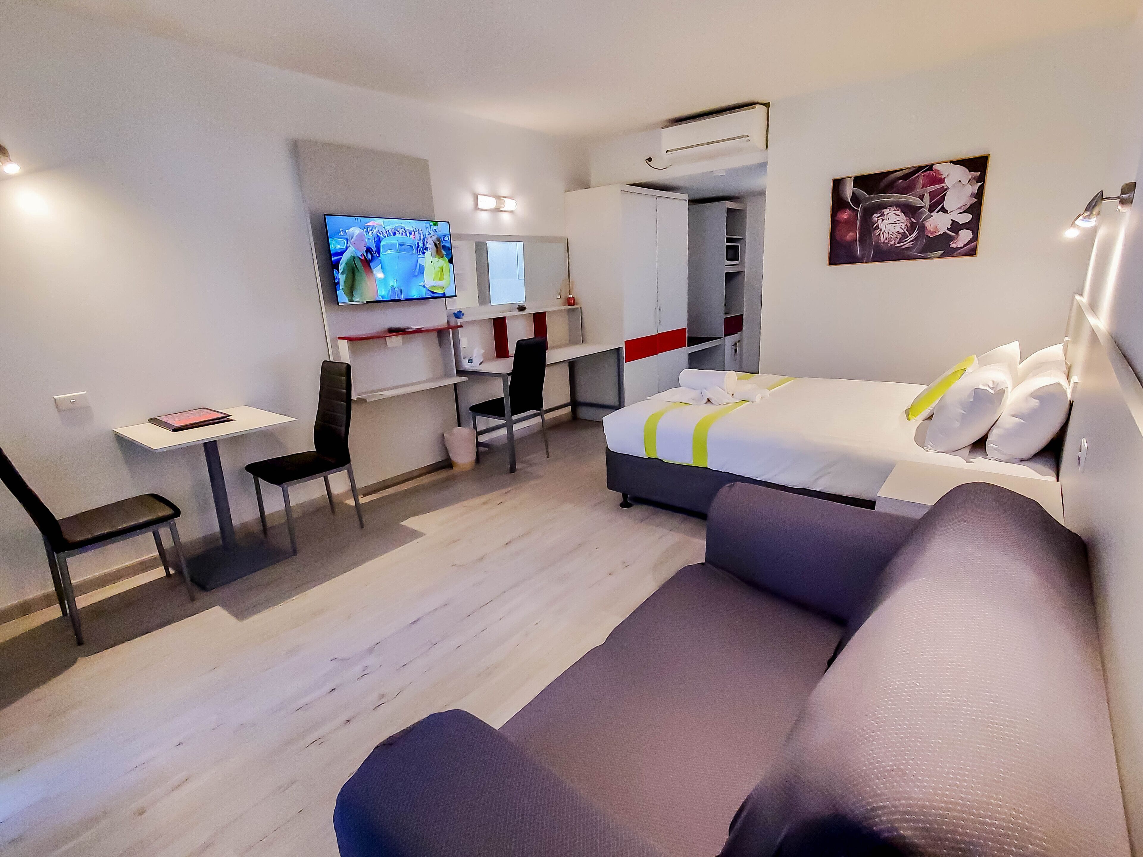 A modern hotel room with a bed, a desk, a chair, a TV, and a painting on the wall.