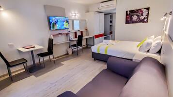 A modern hotel room with a bed, a desk, a chair, a TV, and a painting on the wall.
