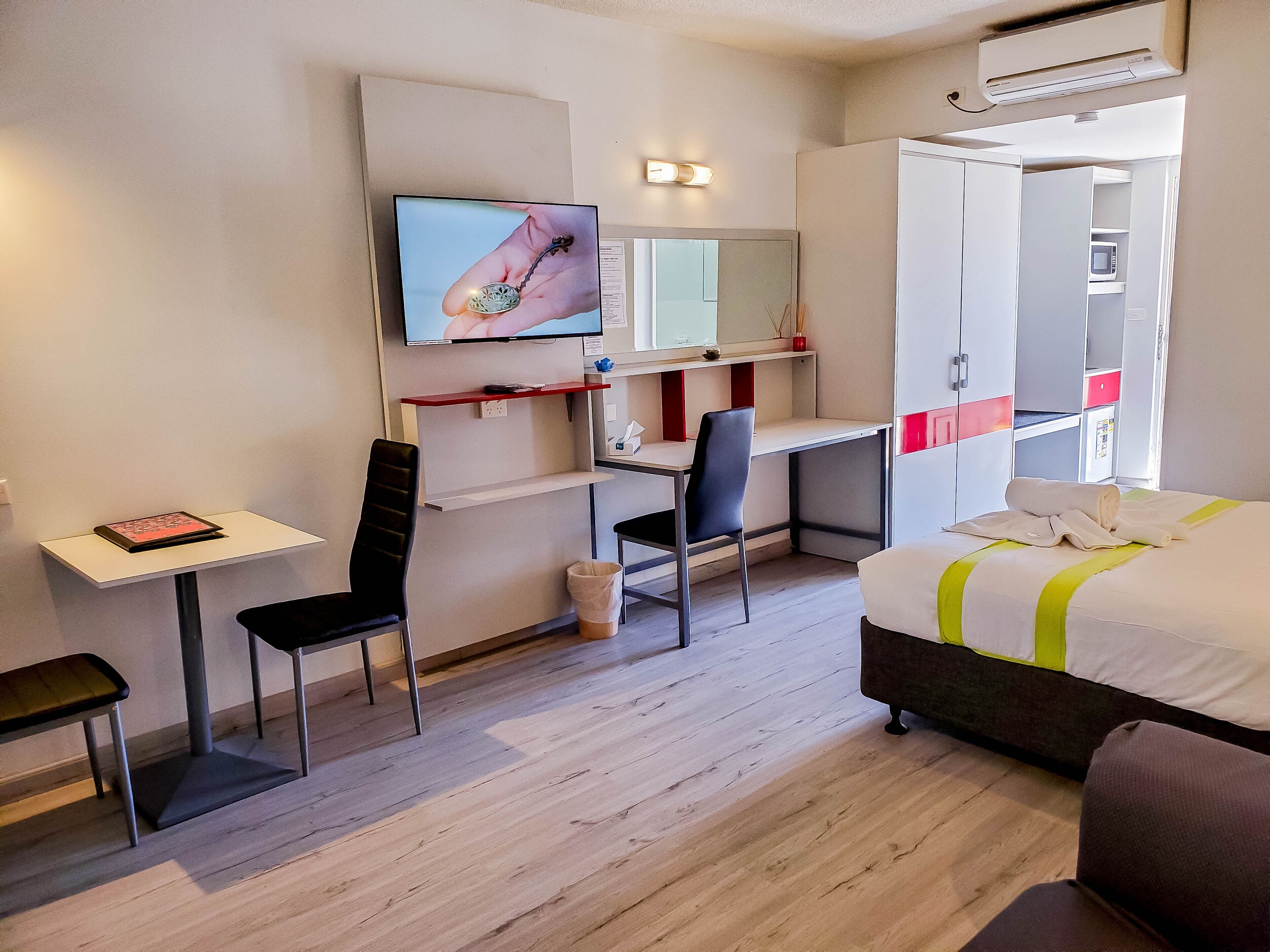 A modern hotel room with a desk, chair, bed, and a television mounted on the wall.