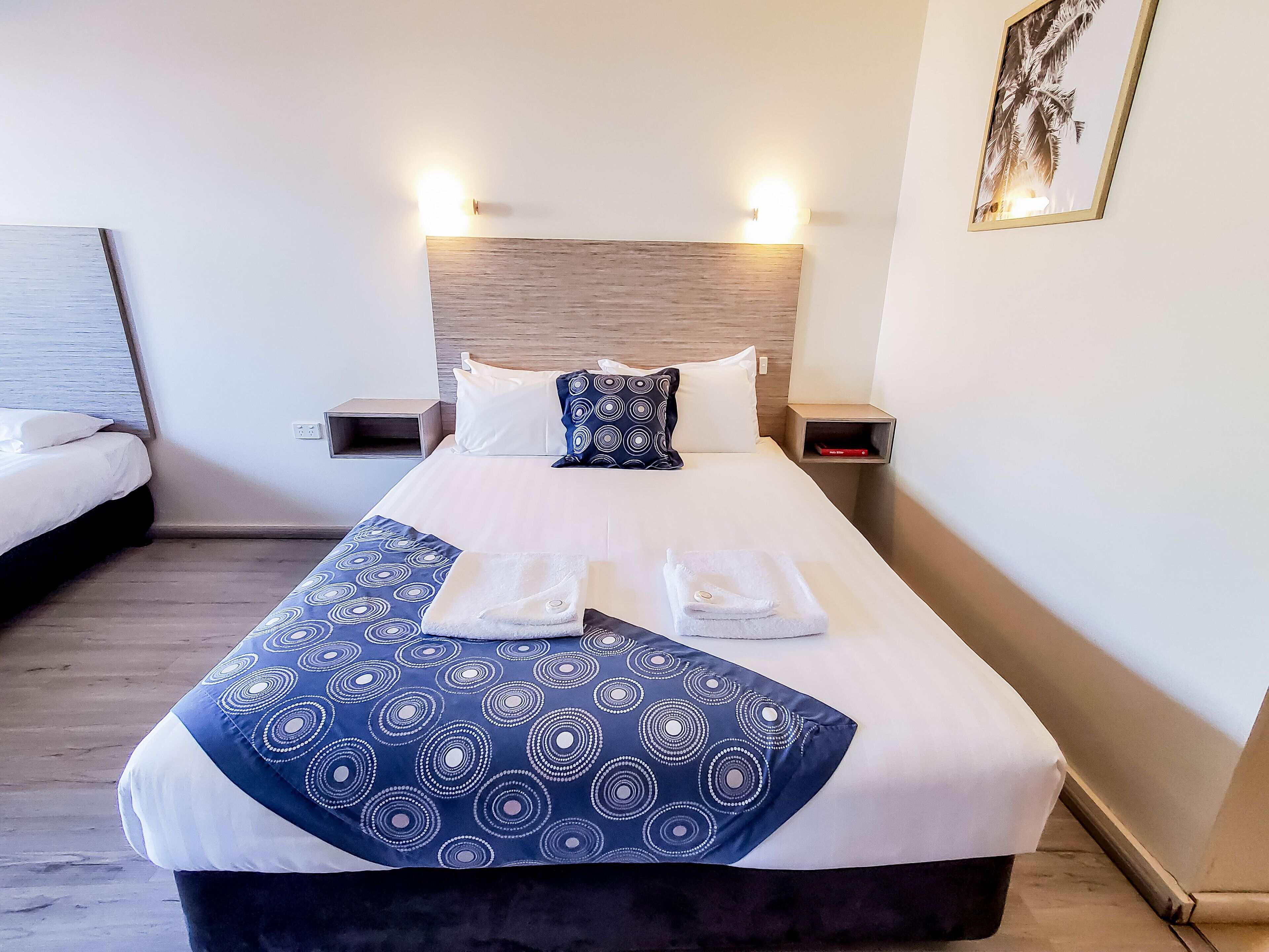 A hotel room with a large bed, two bedside tables, and a headboard with built-in lighting.