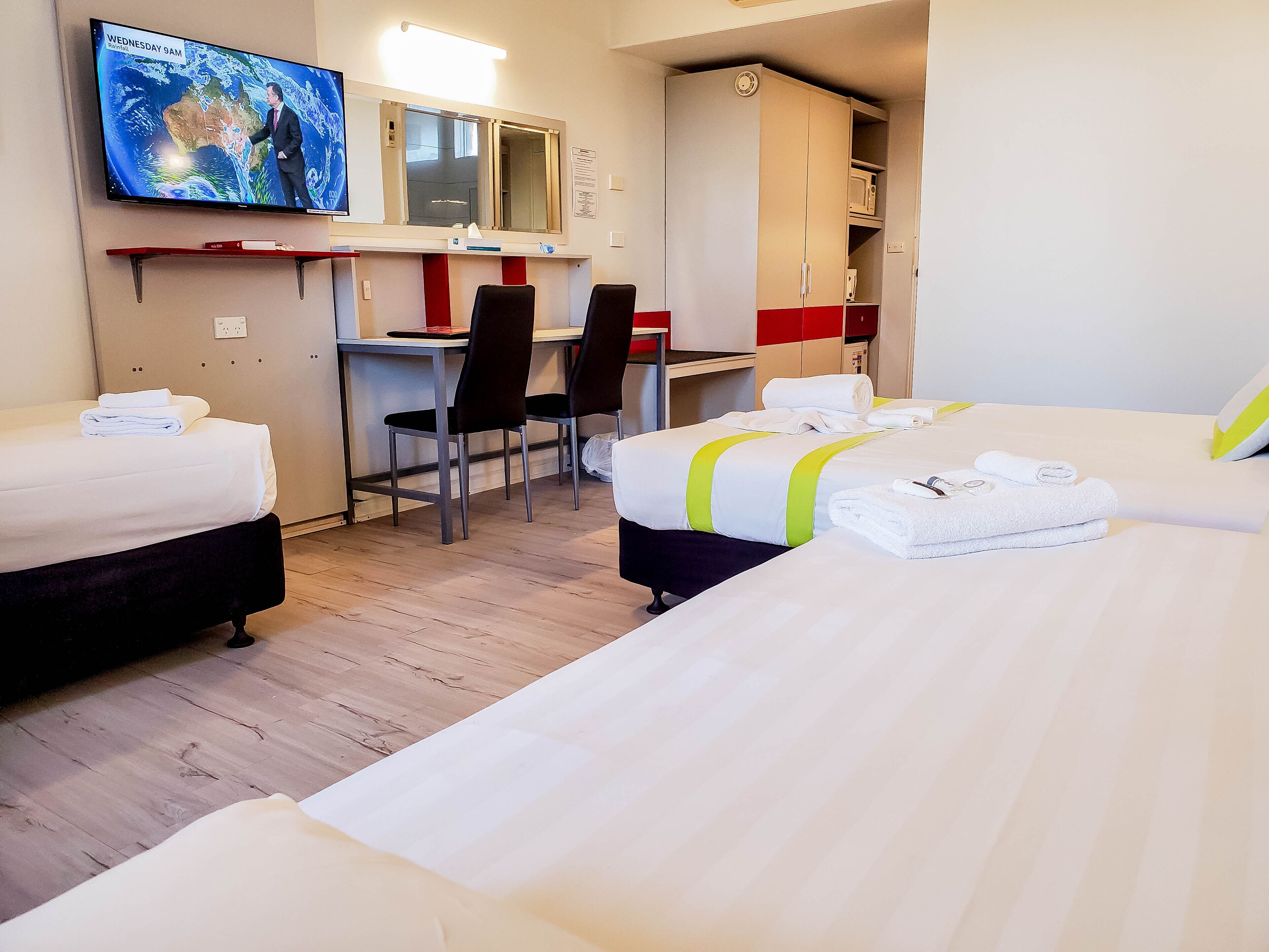 Une chambre d’hôtel avec deux lits, un bureau, des chaises, une télévision et une armoire.