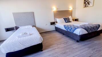 Quarto de hotel com duas camas, cabeceira de madeira, prateleira na parede e um quadro emoldurado.