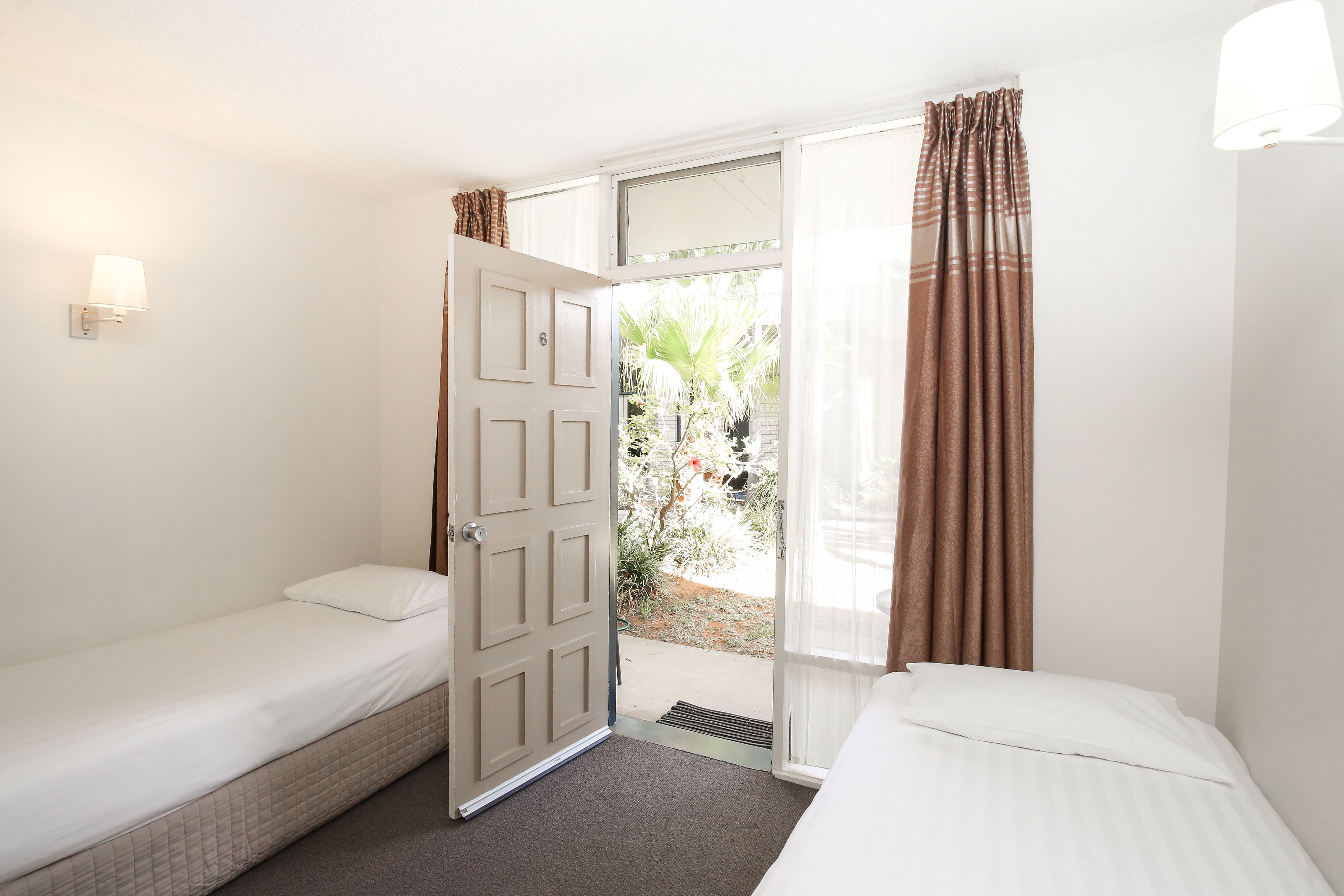 A room with two single beds, a door leading to an outdoor area, and a window with curtains.