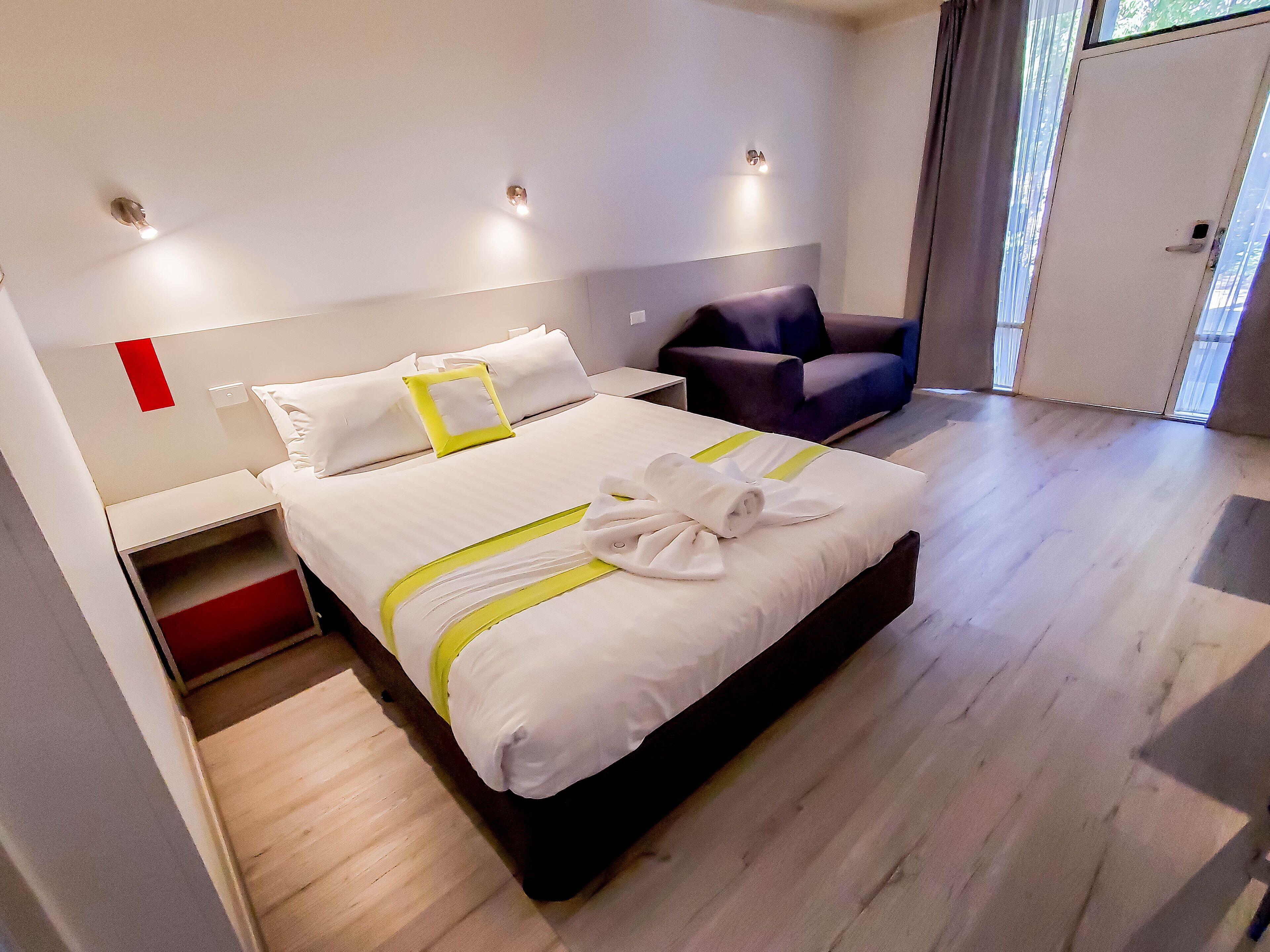 A modern hotel room with a neatly made bed, a chair, and a nightstand.