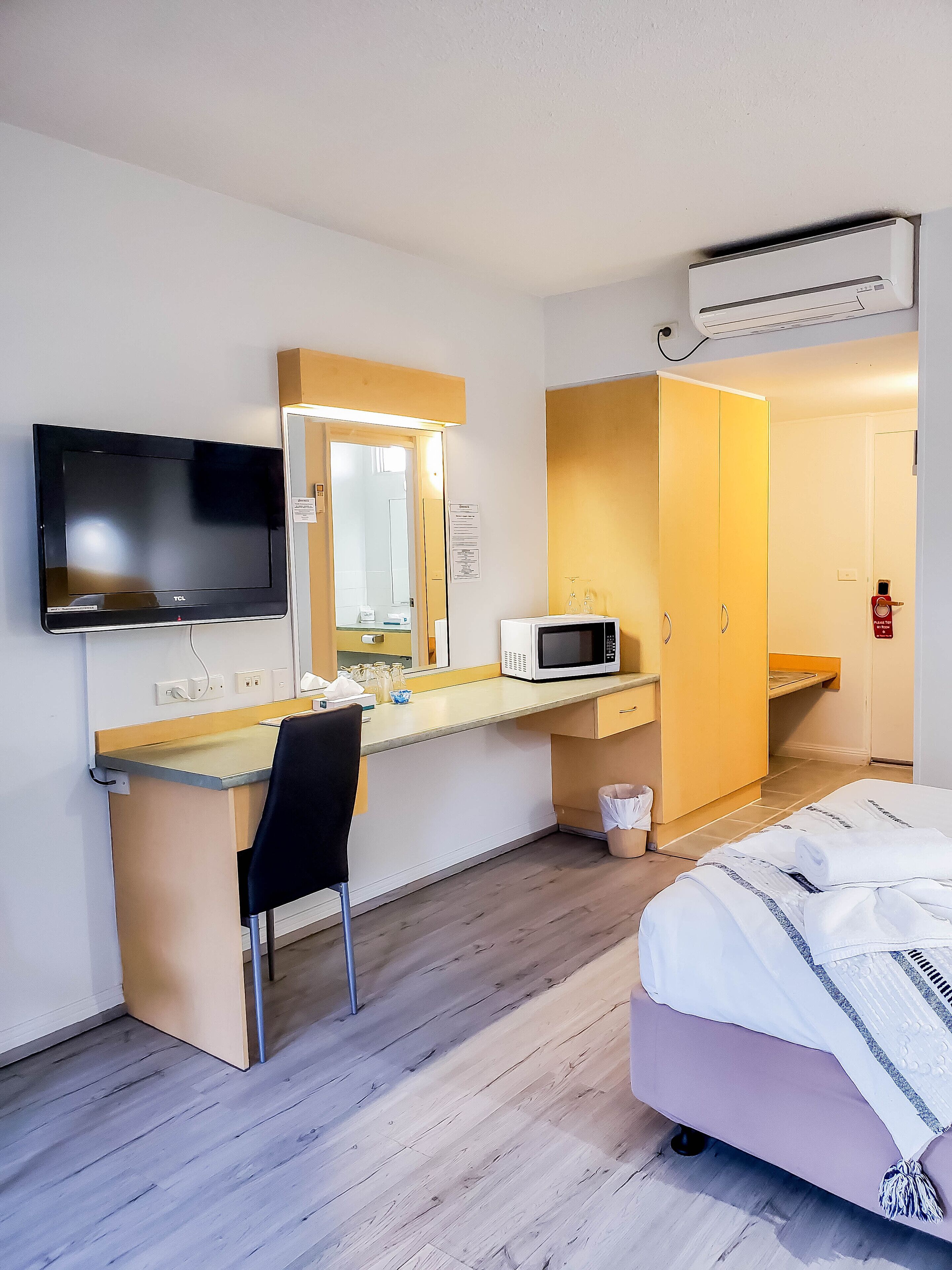 Una habitación de hotel con cama, escritorio con silla, televisor, microondas y armario.
