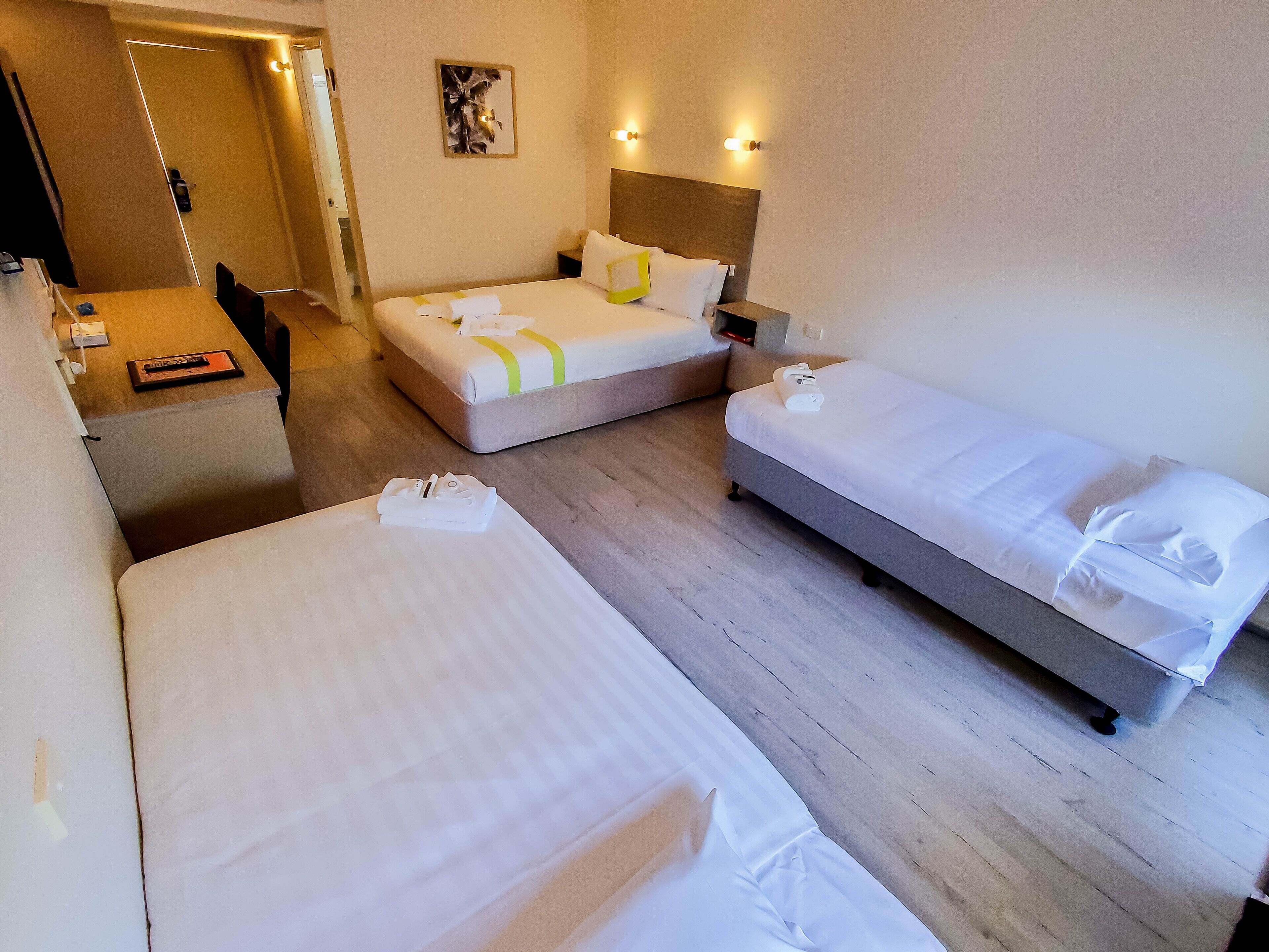 Une chambre d’hôtel avec deux lits, un bureau et une chaise. Il y a un tableau au mur et une porte qui donne sur une autre pièce.