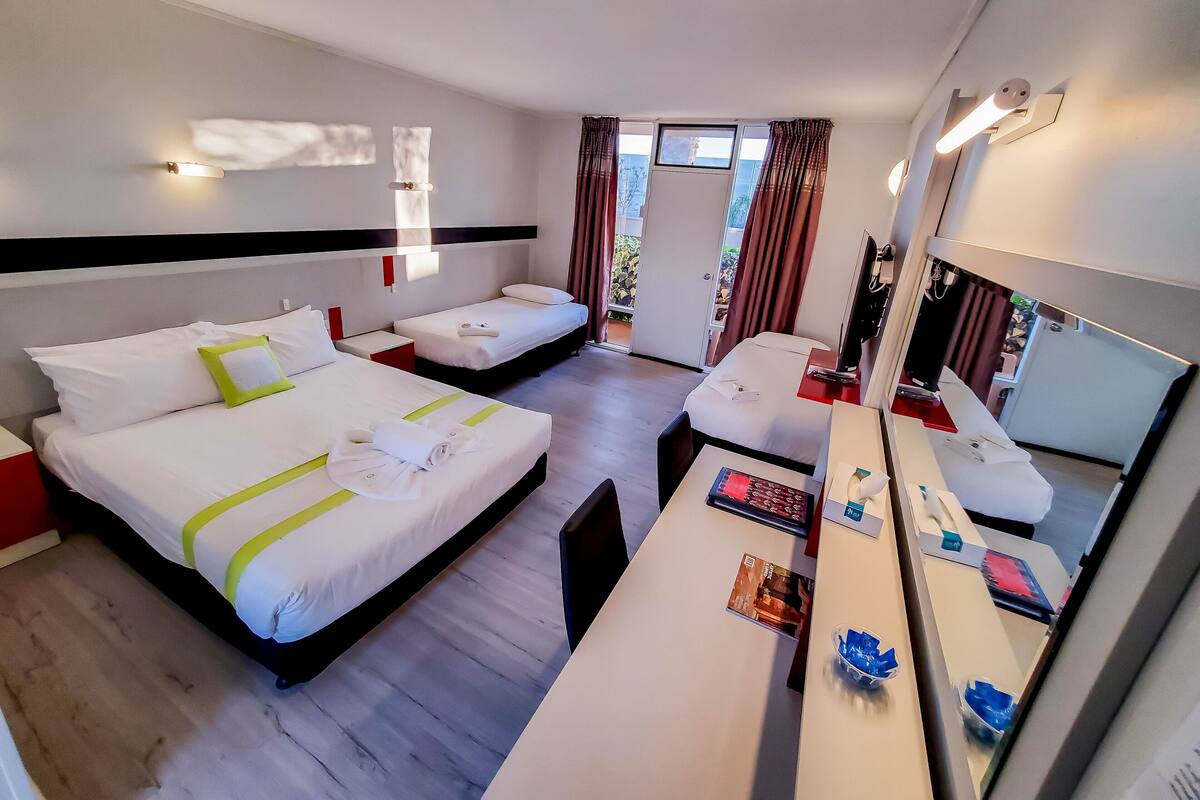 Une chambre d’hôtel avec deux lits, un bureau, un miroir et une fenêtre avec des rideaux.