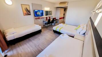 A hotel room with two single beds, a desk, a chair, a TV, and a small kitchenette.