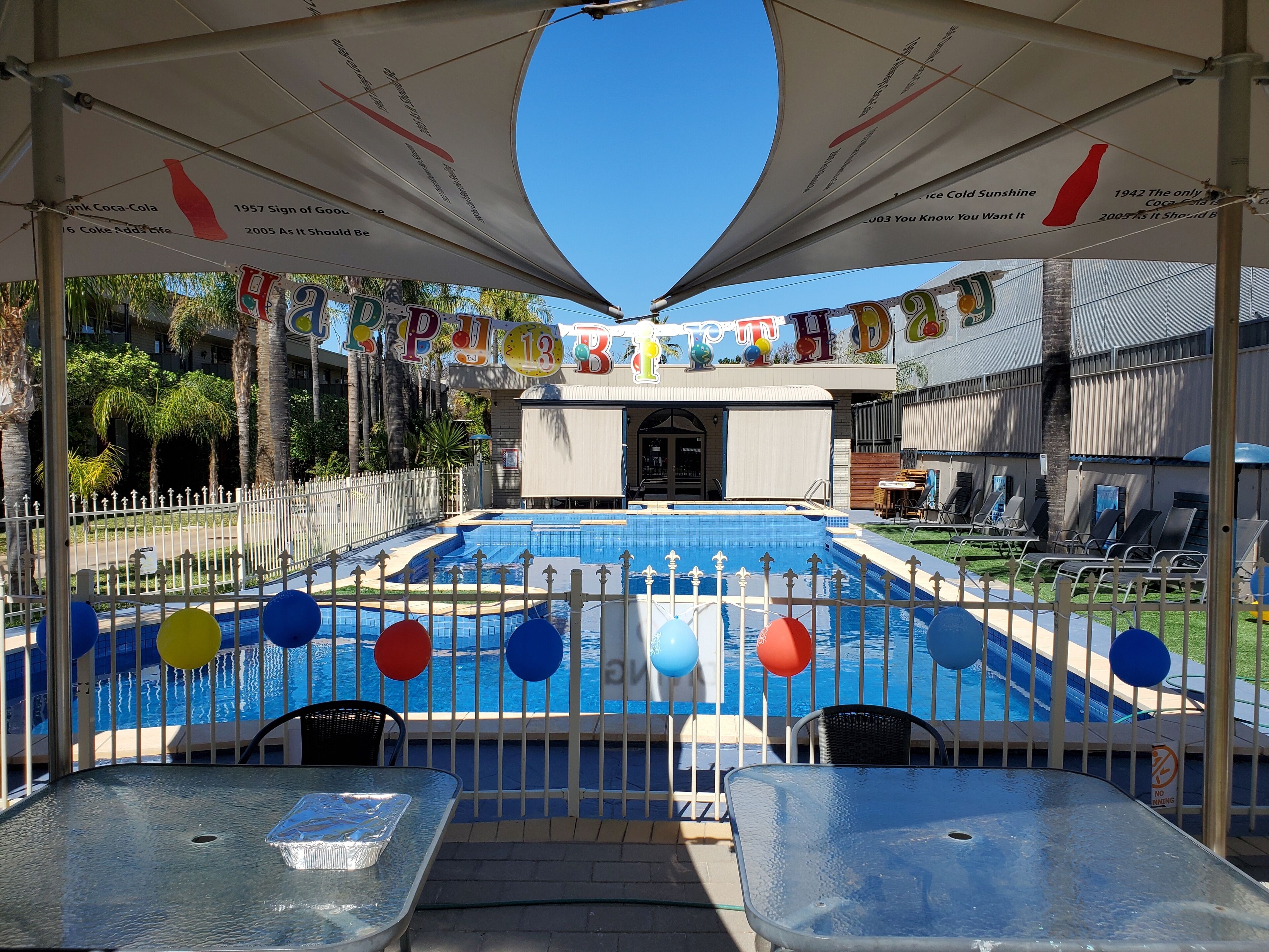 A pool area with a covered seating area, a fence, and a banner with colorful letters.