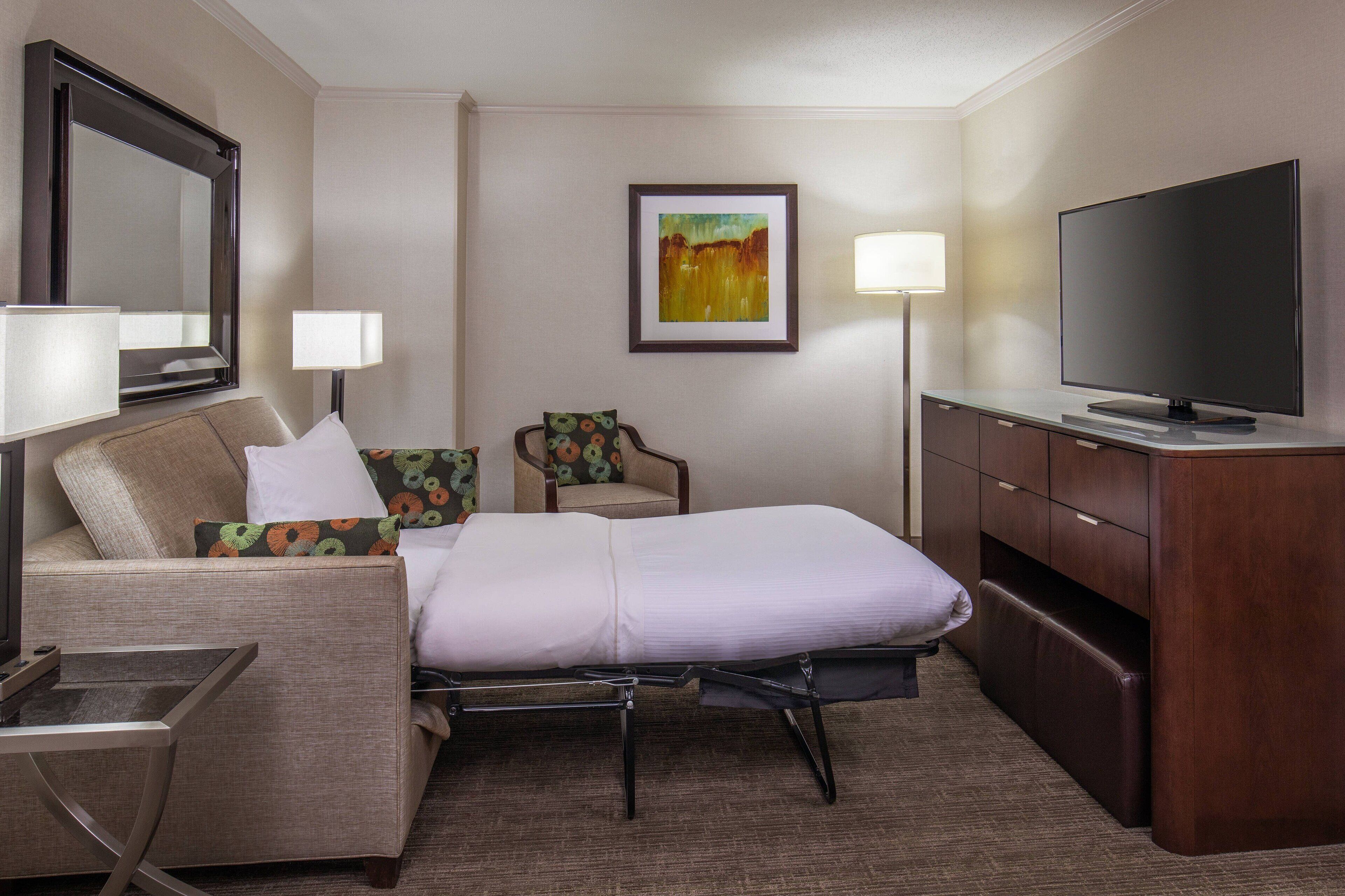 Ein Hotelzimmer mit Bett, Schreibtisch, Stuhl, Fernseher und einem Bild an der Wand.