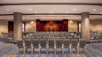 A conference room with rows of chairs, a stage, and a carpeted floor.