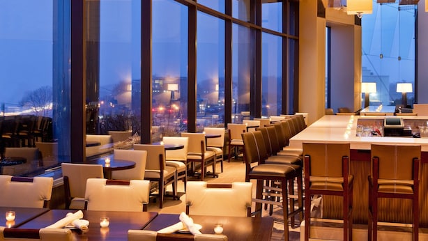 A modern restaurant with large windows, leather seating, and a bar area. - The Westin Waltham-Boston (Waltham)