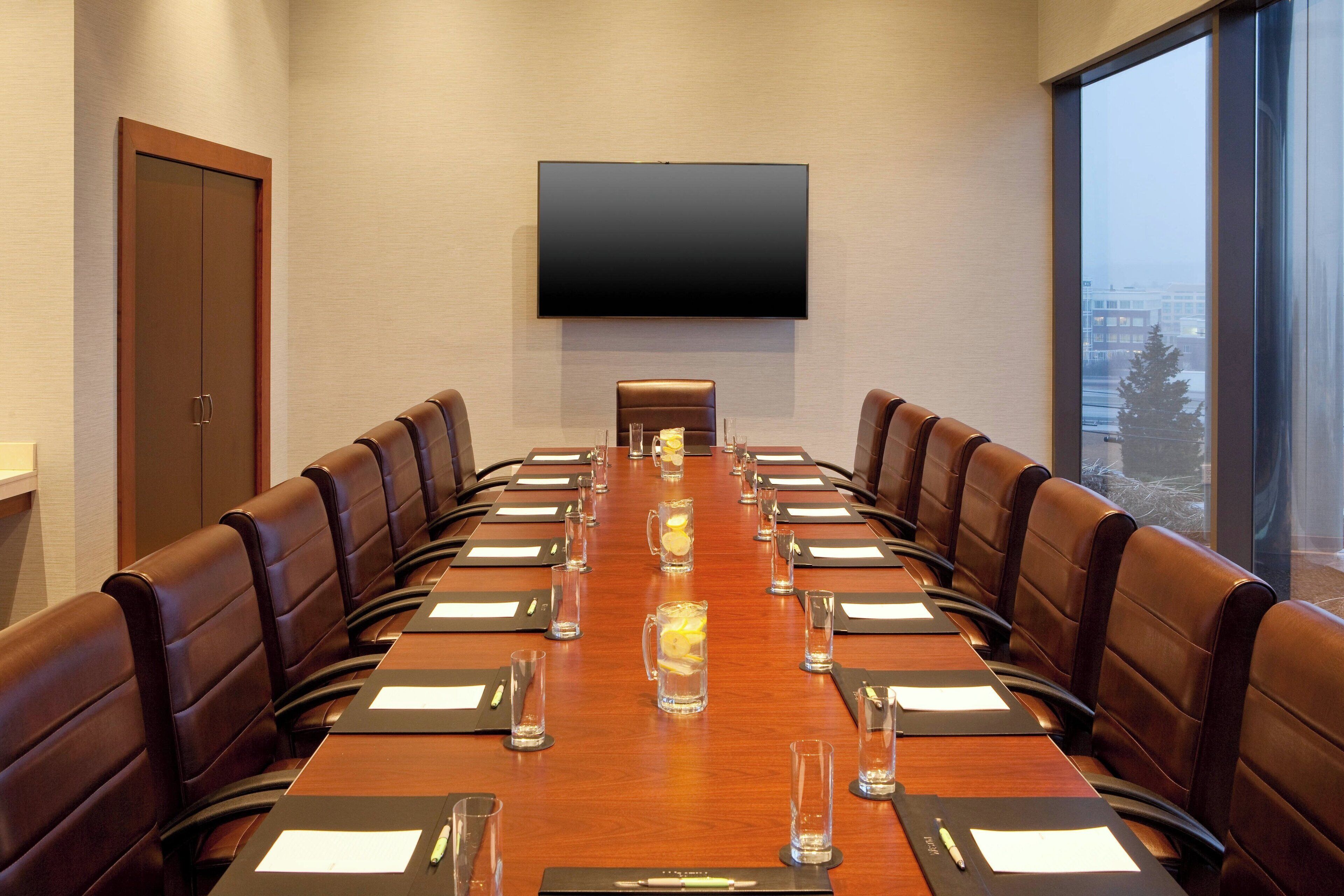 A conference room with a long table, leather chairs, and a large flat-screen TV on the wall.