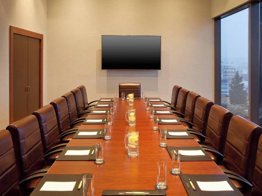 A conference room with a long table, leather chairs, and a large flat-screen TV on the wall.