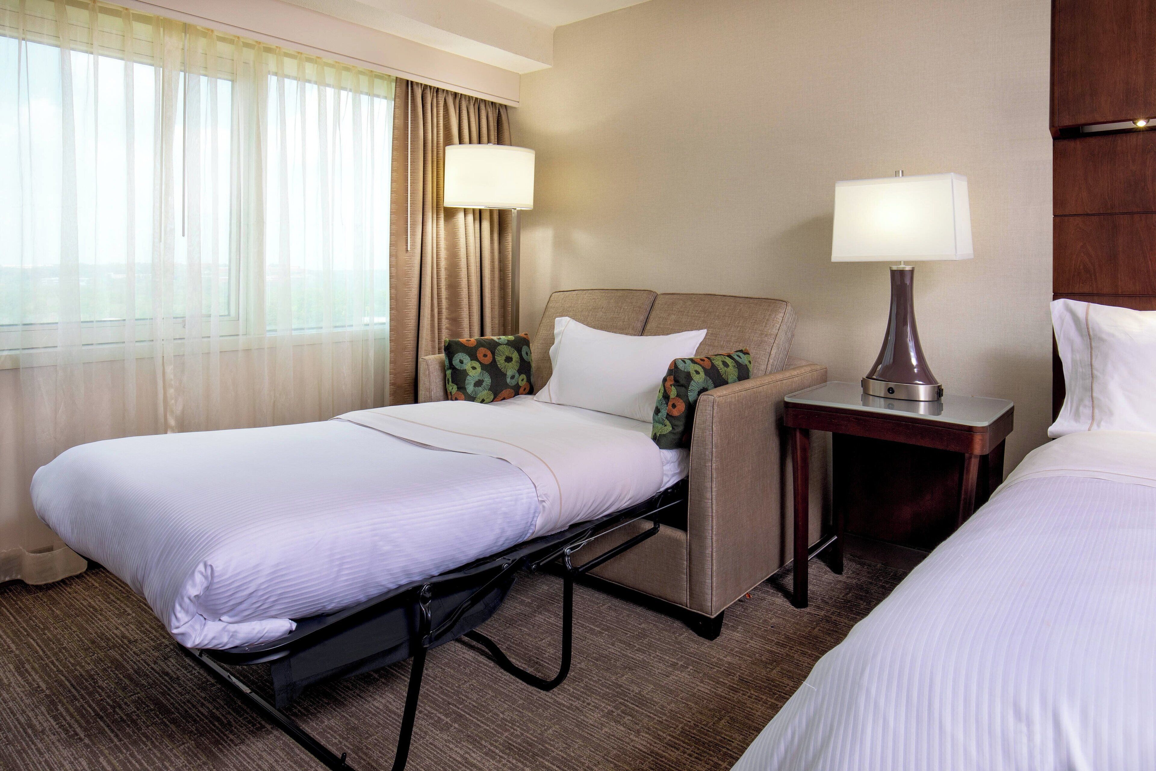 A hotel room with a bed, a chair, a nightstand, and a lamp.